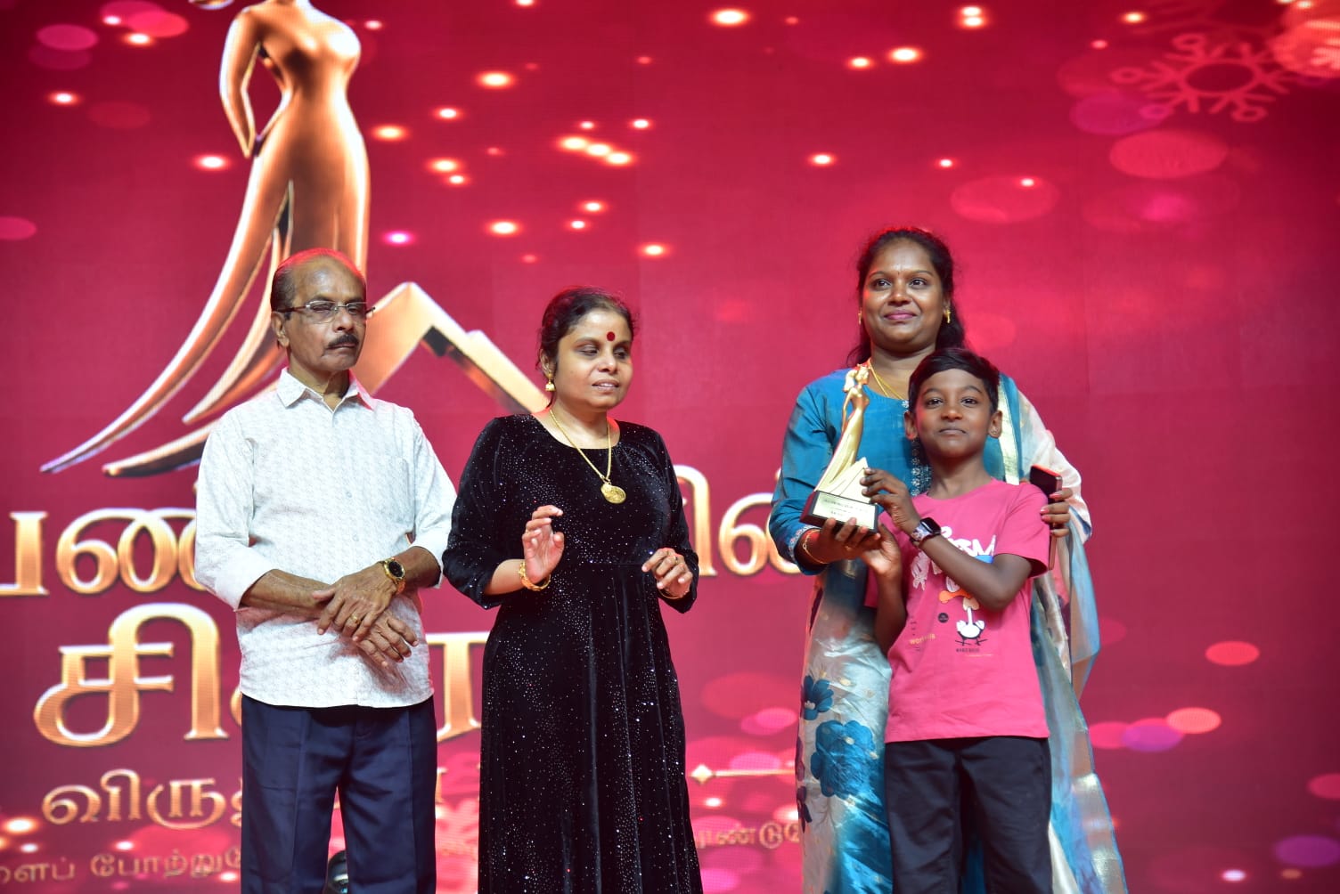 Vikom Vijayalakshmi holding her award on stage with her family